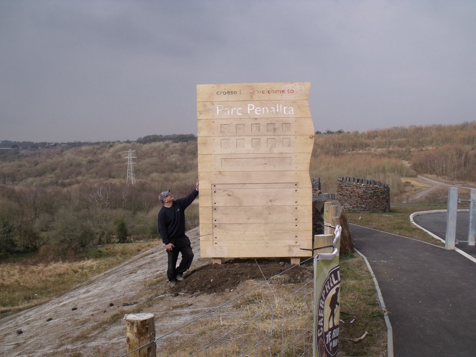 Tall timber structure being built on an open hillside, with a person standing beside it for scale