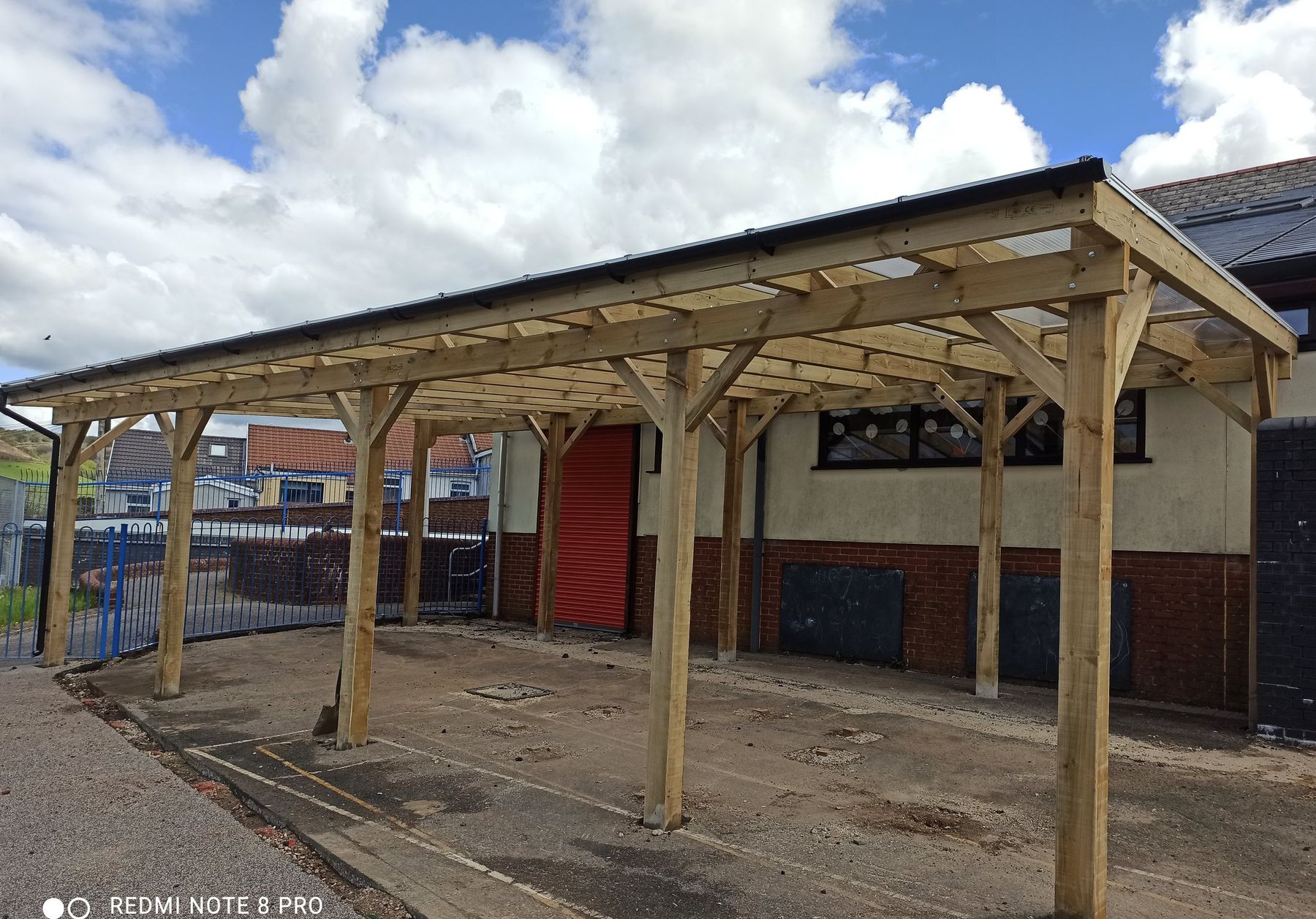 Long timber canopy on posts running along a school building, sheltering the playground