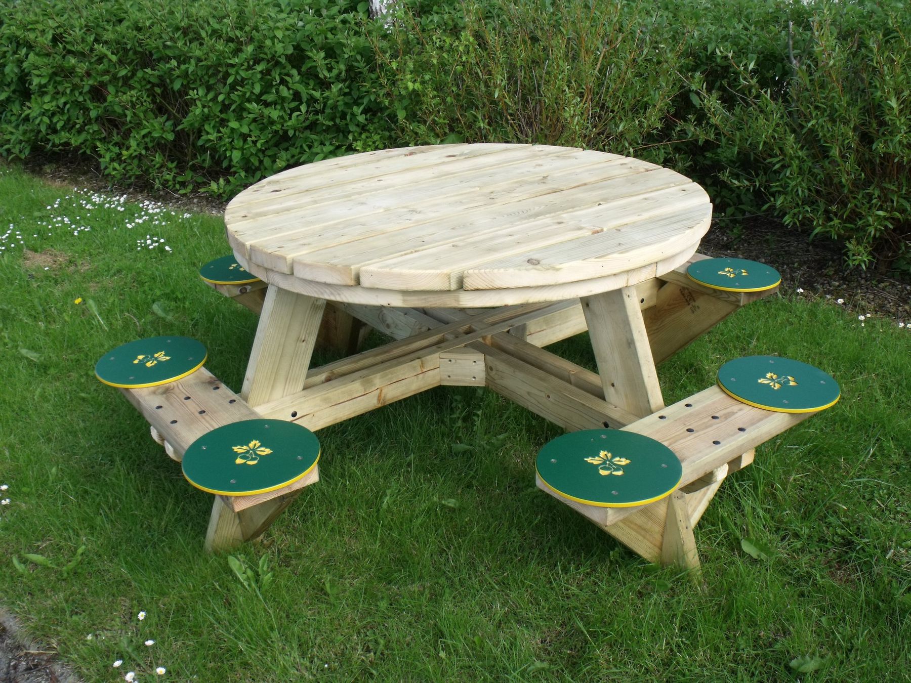 Round timber picnic table with green-painted stools on grass