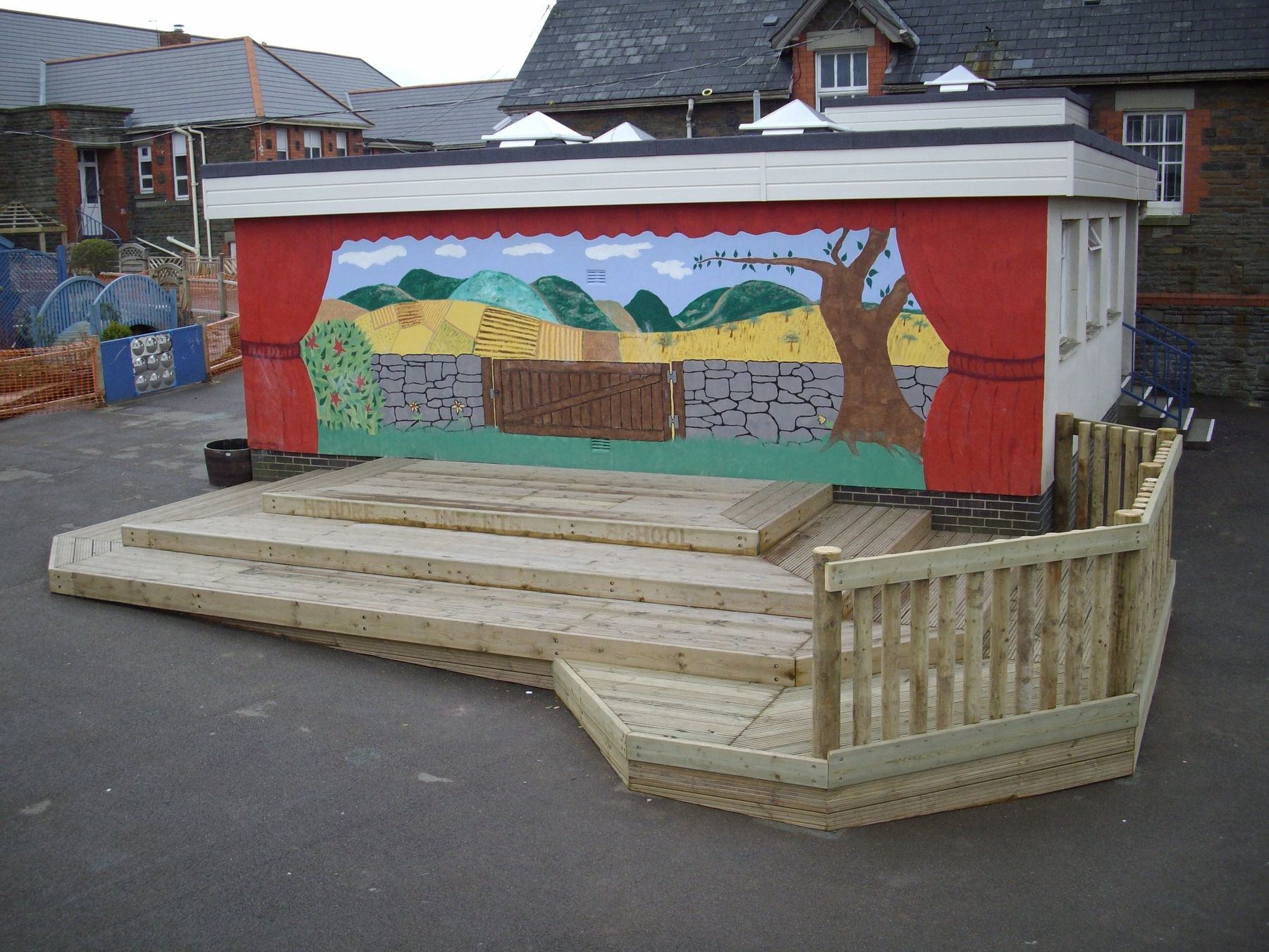 Timber stage with tiered steps in front of a painted mural backdrop in a school playground