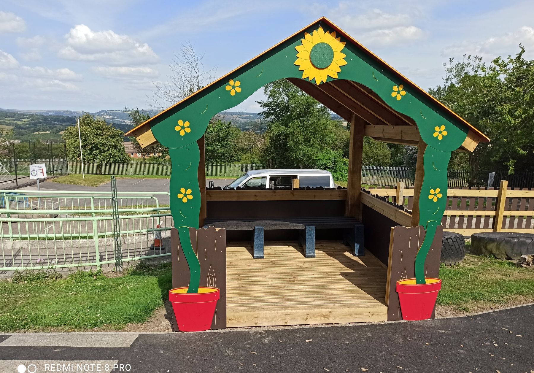 Timber play hut with a green and yellow painted frame and sunflower decorations