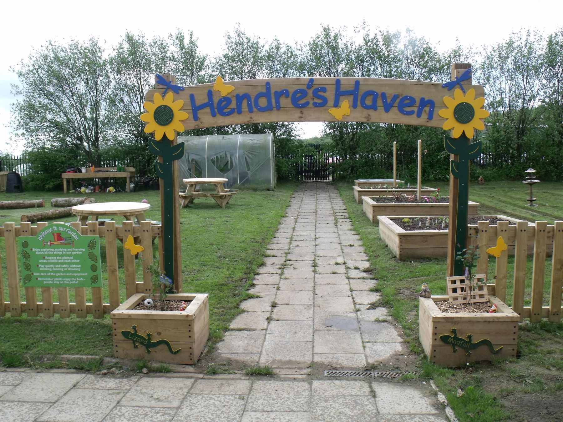 Timber entrance arch carved Hendre's Haven with sunflowers, over a path lined with timber planters