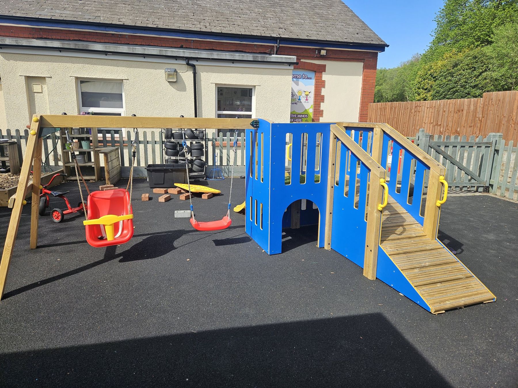 Colourful timber climbing frame with a ramp and swings on safety surfacing