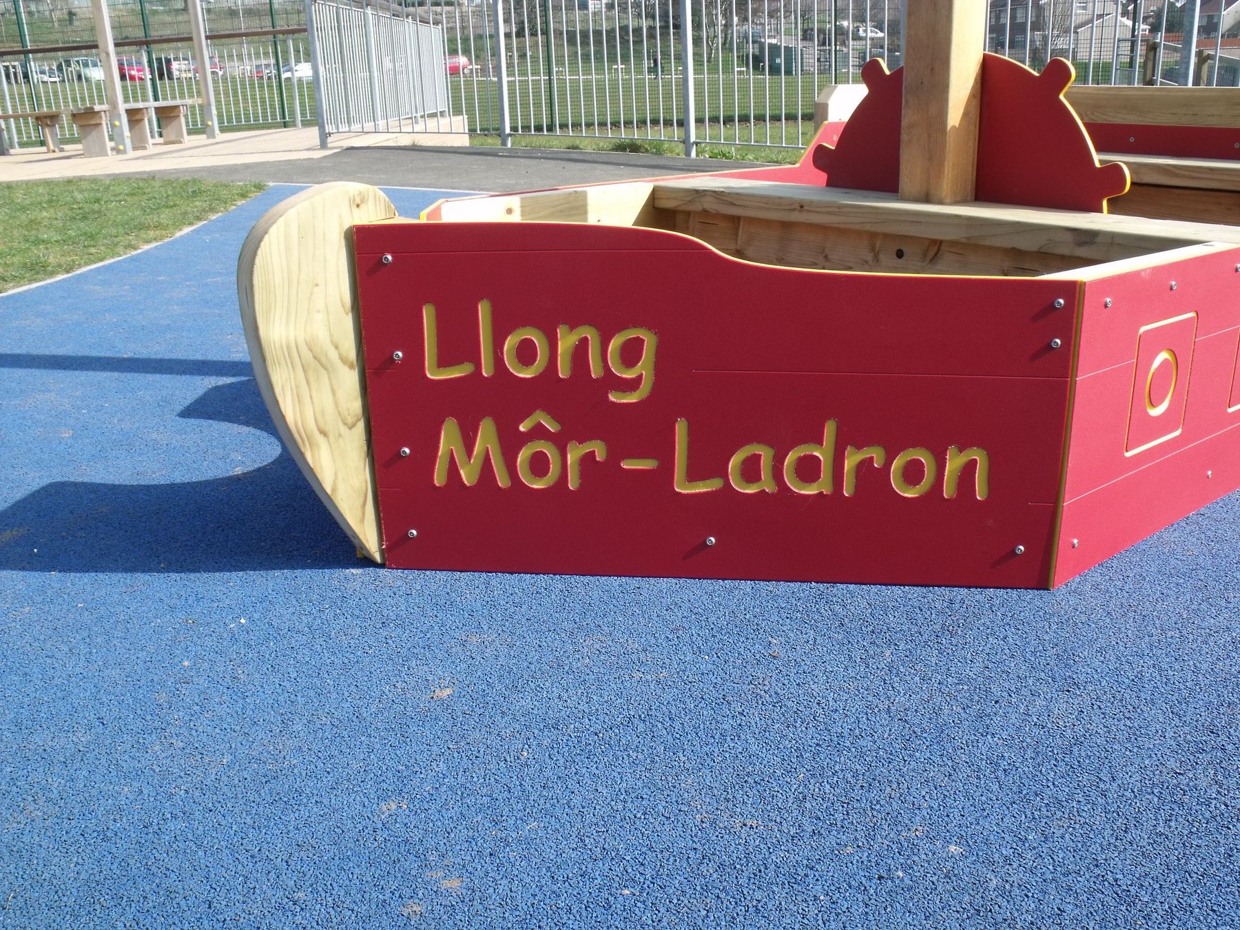 Red timber pirate ship play structure carved Llong Môr-Ladron, on blue safety surfacing