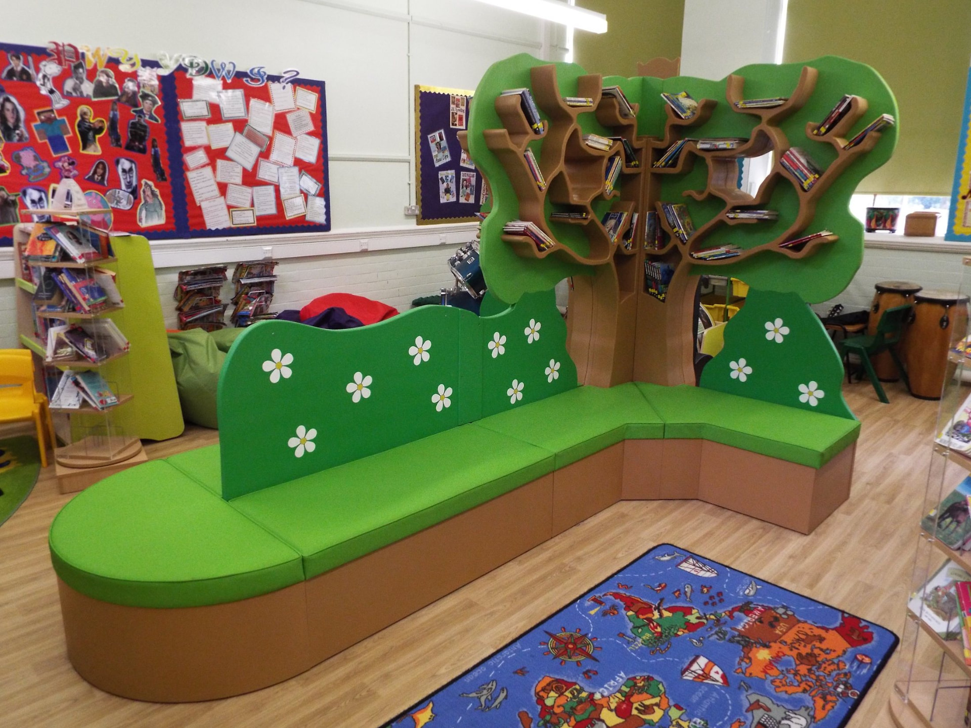 Indoor reading corner with a large tree-shaped timber bookshelf and green cushioned seating