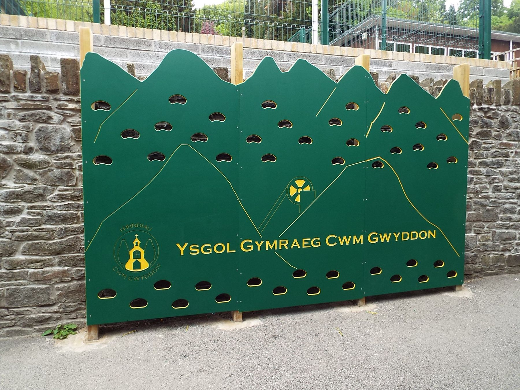 Green timber panel carved Ysgol Gymraeg Cwm Gwyddon, with handholds and a mountain outline