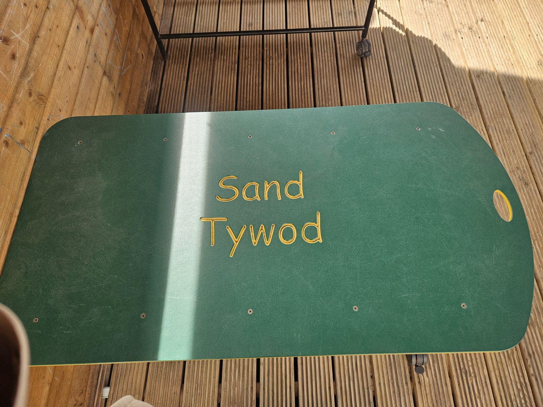 Green timber sandpit lid carved with the words Sand and Tywod