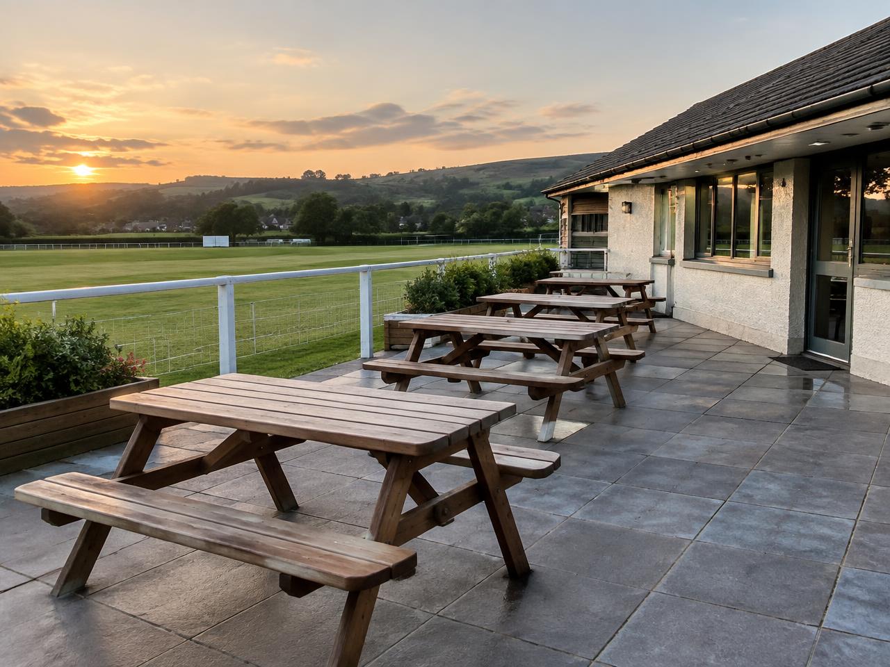 Illustrative timber picnic benches on a clubhouse terrace overlooking a Welsh playing field