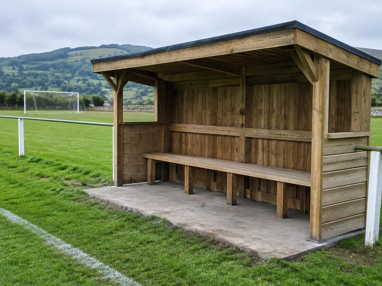 Illustrative timber team dugout with bench at the edge of a Welsh football pitch