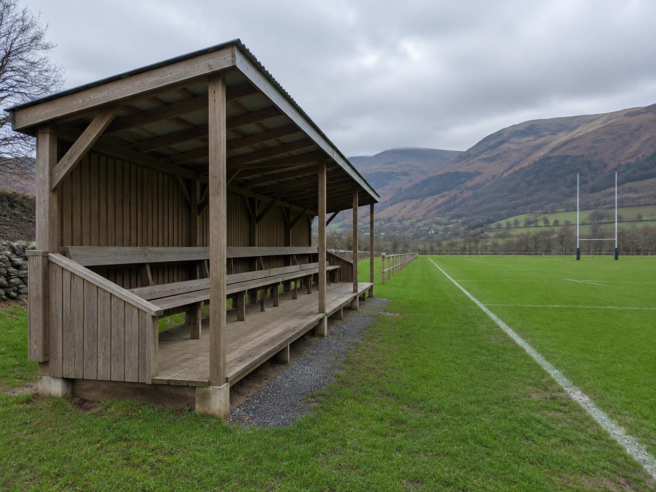 Illustrative covered timber spectator stand beside a Welsh rugby pitch